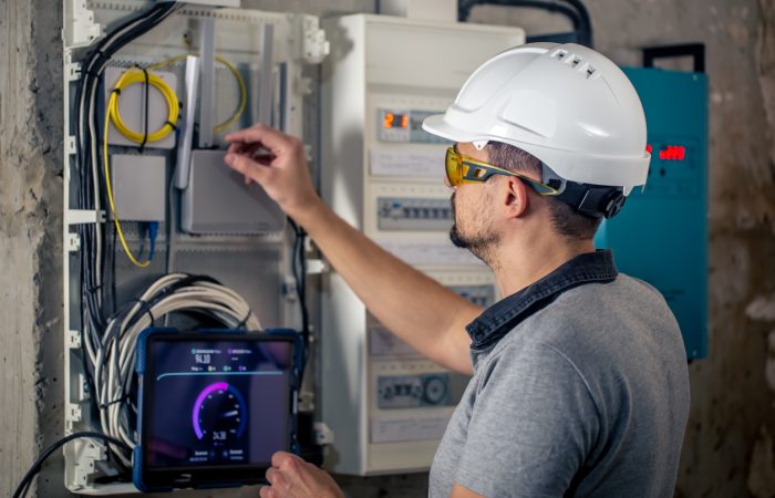 Man, an electrical technician working in a switchboard with fuses. Installation and connection of electrical equipment. Professional uses a tablet.